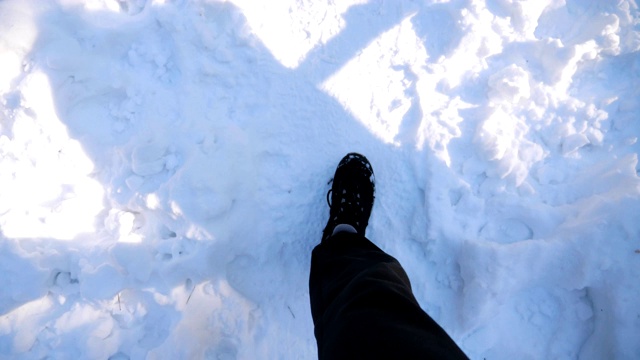 在雪道上行走的男性脚的俯视图。穿着靴子的人走在路上，踩在洁白的雪地上。难以辨认的徒步旅行者在森林中漫步。冬天的概念。POV慢动作特写视频素材