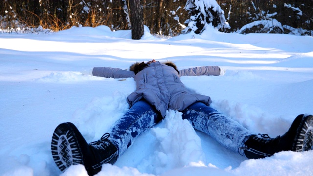 面目全非的年轻女孩躺在雪甸上做天使。快乐的女人在雪地里玩，享受冬天的时光。快乐的女士在户外玩。寒假的概念。慢动作特写视频素材