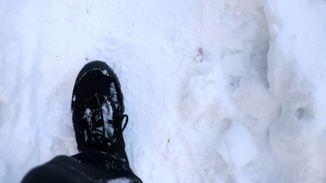 在雪道上行走的男性脚的细节视图。穿着靴子的人走在路上，踩在洁白的雪地上。难以辨认的徒步旅行者在森林中漫步。冬天的概念。POV慢动作接近顶部视图视频素材