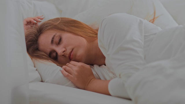 漂亮的年轻女子正在卧室的床上酣睡。有白色枕头和毯子的舒适房间。肖像的观点。视频素材