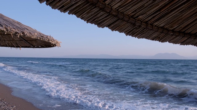 海景海洋和美丽的海景热带海滩透过茅草伞。空旷的沙滩上的背景清澈的绿松石海。节日的概念视频素材