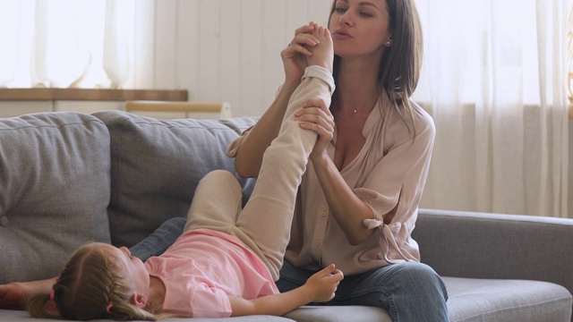 快乐的年轻妈妈和可爱的女儿在沙发上玩视频素材