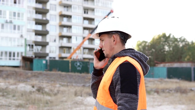 成功的建筑工程师，建筑师戴着白色的头盔，在建筑工地打电话视频素材