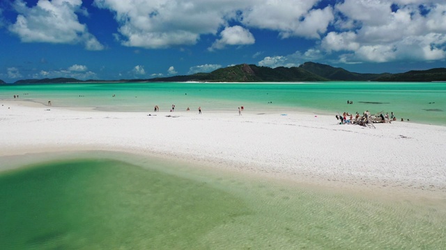 鸟瞰游客在白色港湾海滩的硅砂和绿松石海水中玩耍。视频素材