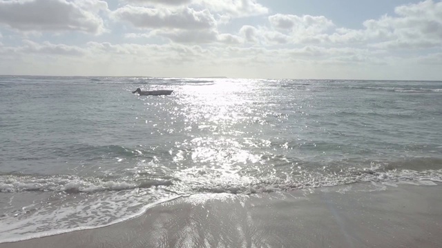 一艘孤立的船在海浪上撞击海岸与太阳反射的背光和多云的天空拍摄在平坦的颜色轮廓的缓慢运动视频素材