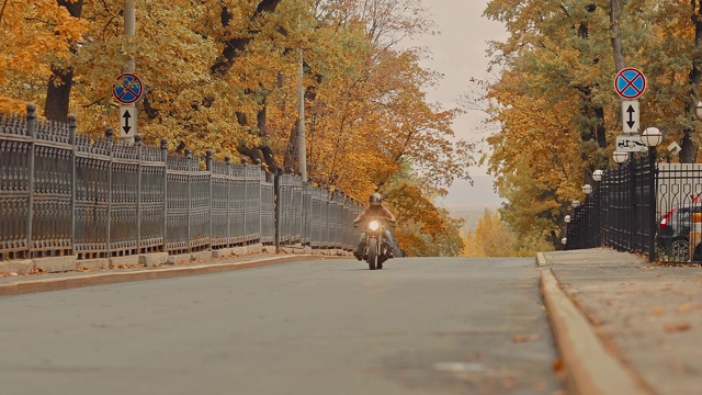 骑自行车的人在秋天离开了公路。一个残忍的人骑着一辆很酷的摩托车，戴着头盔。视频素材