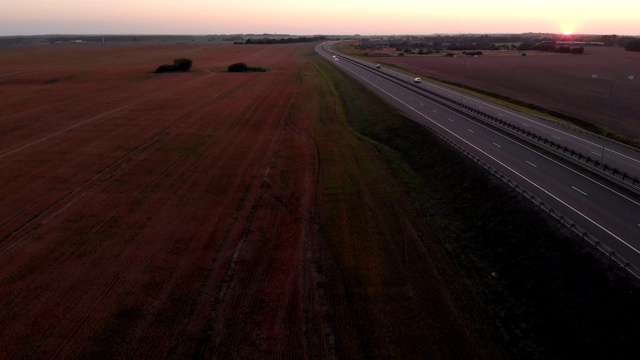 许多汽车是移动的夕阳。空中拍摄的车辆在美丽的乡村道路在日落。鸟瞰道路上的汽车与日落的背景。视频素材