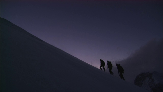 登山运动员艰难地爬上白雪覆盖的山坡。视频素材