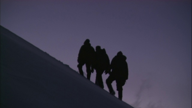 登山运动员艰难地爬上白雪覆盖的山坡。视频素材