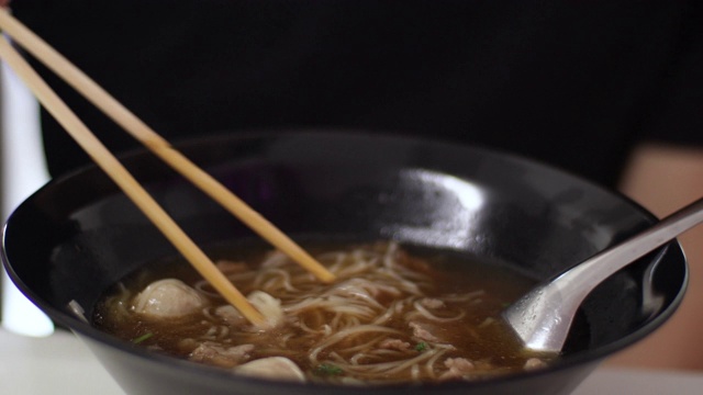 4k近距离亚洲人在餐厅吃牛肉面，热汤，面条碗，午餐，肉丸炖牛肉，清汤，餐厅，穿着黑色t恤视频素材