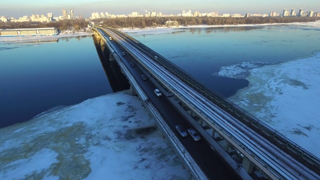 汽车行驶在横跨冬季河流的公路大桥上。鸟瞰图冬季城市视频素材