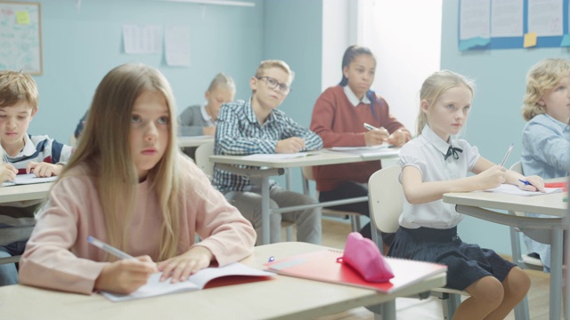 多元聪明的孩子们用心听老师讲课的小学课堂。学校里聪明的孩子们用练习本写作，参加考试。人像视图移动摄像机视频素材