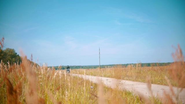 一个骑摩托车的男人在麦田上方尘土飞扬的乡间道路上骑着摩托车视频素材