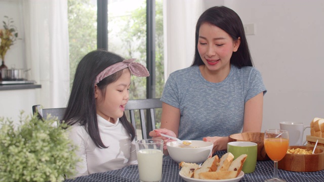 日本亚裔家庭在家里吃早餐。亚洲的妈妈，爸爸和女儿感到愉快的谈话在一起吃面包，玉米片，谷物和牛奶碗在厨房的桌子上在早上。视频素材