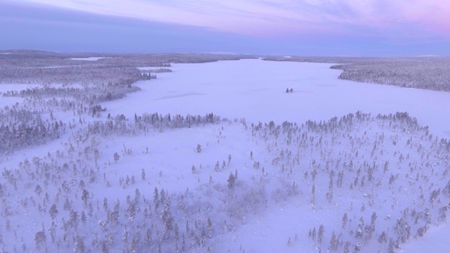 在冬季日落时被雪覆盖的森林和湖泊，托拉西比湖，芬兰拉普兰，芬兰，欧洲的无人机视频素材