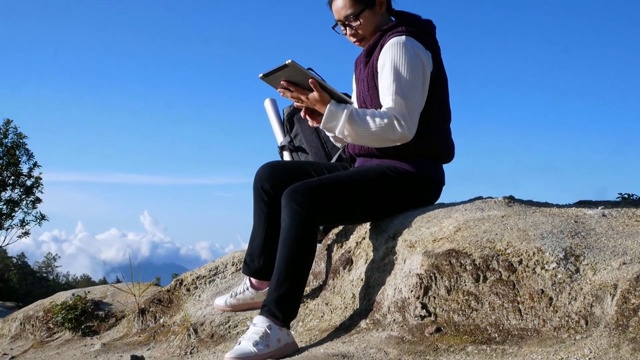 暑假，一名年轻的女游客在山顶用平板电脑搜索GPS坐标。科技和旅游的概念。视频素材