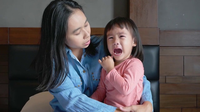 一位亚洲母亲把她哭泣的小女儿抱在怀里，试图让她在床上平静下来。视频素材