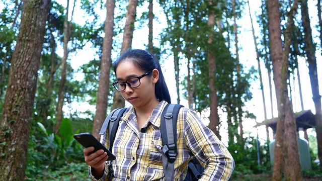 年轻女子旅行者在夏季假期的自然小径上通过手机搜索GPS坐标。徒步旅行生活方式的概念。视频素材