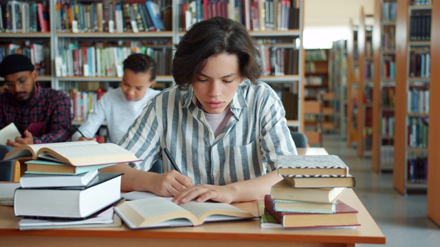 一个疲惫的男孩在大学图书馆书桌前看书学习的慢镜头视频素材