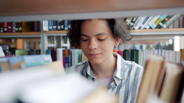 特写英俊的十几岁的男孩学生选择在大学图书馆的书视频素材