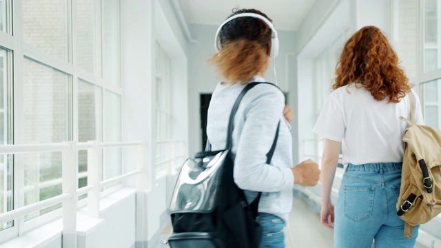 戴着耳机的快乐女孩在大学大厅里唱歌跳舞视频素材