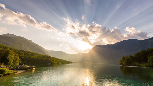 Bohinj湖,斯洛文尼亚。时间推移的视频日落以上的湖泊与戏剧性的移动云。太阳在山峦和宁静的水面上耀斑。人们和船在湖中。Triglav国家公园。视频素材