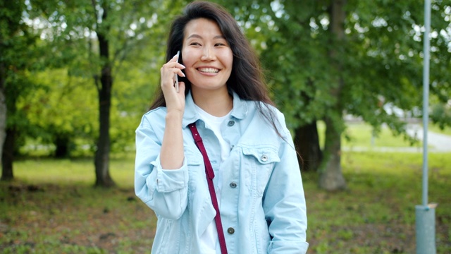 快乐的亚洲女人在城市公园的户外打电话微笑视频素材