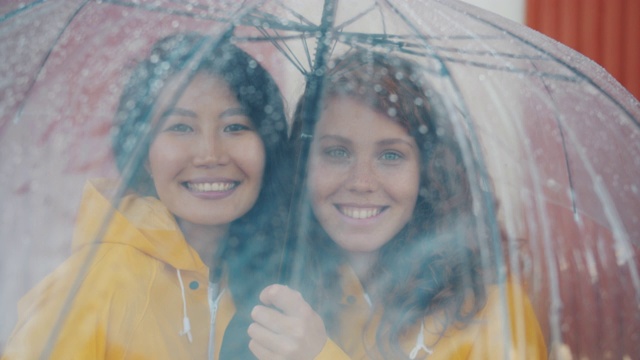 快乐的朋友们穿着雨衣站在户外的雨伞下视频素材