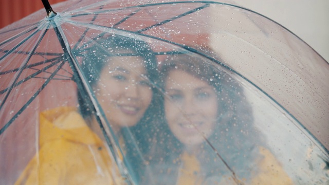 特写的漂亮女孩在雨伞下站在一起微笑雨衣视频素材