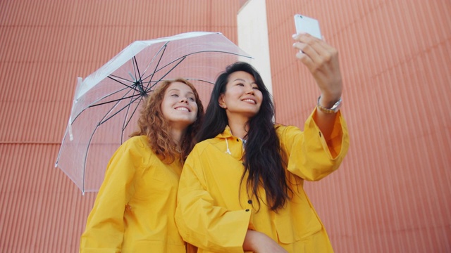 女孩们穿着雨衣打着雨伞在户外自拍视频素材