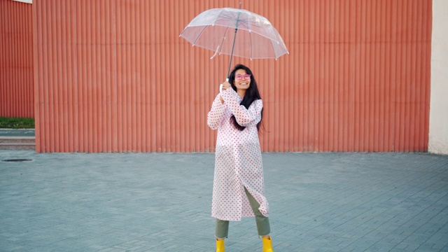 慢动作的亚洲妇女在雨衣和橡胶靴子跳舞与伞视频素材