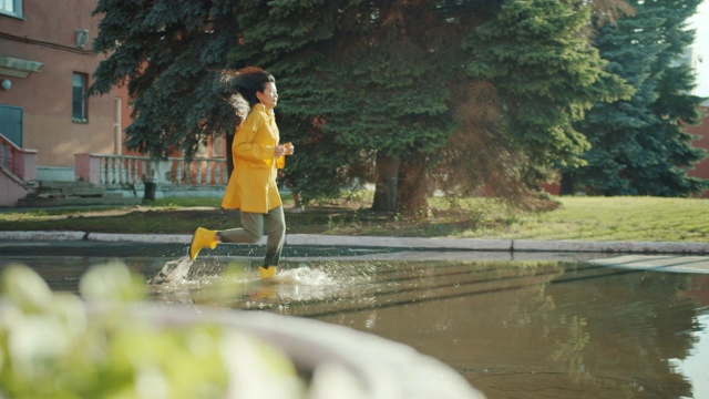 美丽的亚洲女人在水坑里跑步穿着湿衣服，雨衣，橡胶靴视频素材