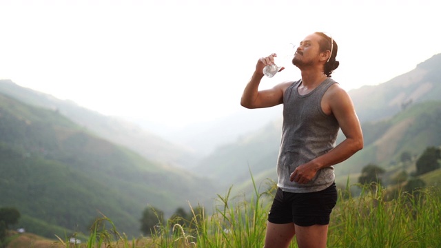 健身男子饮用瓶子里的水，在海滩上跑步锻炼后往脸上泼水降温视频素材