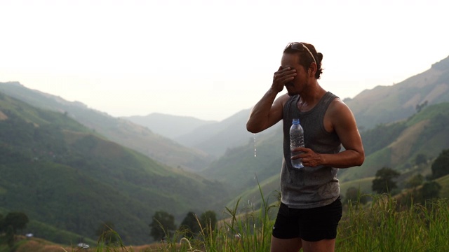 健身男子饮用瓶子里的水，在海滩上跑步锻炼后往脸上泼水降温视频素材