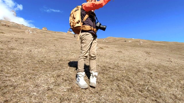 一个快乐的女孩旅行者摄影师的肖像，戴着帽子和太阳镜，脖子上挂着相机，手里拿着手机，以山为背景，用他的智能手机拍照。视频素材