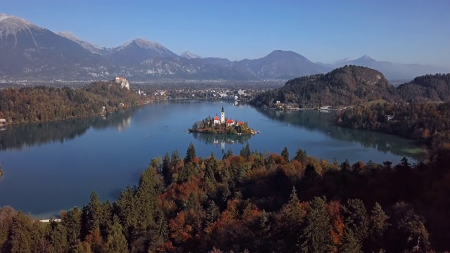 在斯洛文尼亚晴朗的一天，飞往布莱德岛(Blejski otok)与朝圣教堂的圣母升天湖上流血彩色秋天森林视频素材