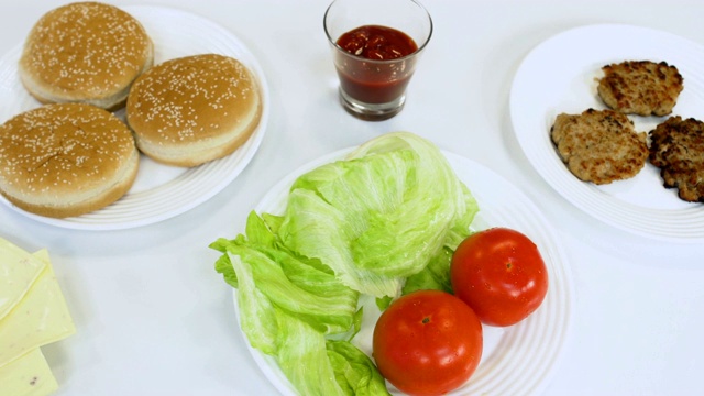 自制汉堡的配料有炸牛肉饼、番茄酱或沙司、新鲜番茄、绿色生菜沙拉、芝麻面包、加工过的奶酪视频素材