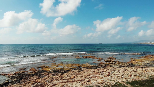 海浪撞击岩石海滩的航拍照片。蓝天和地平线上的白云。晴朗多风的一天，在塞浦路斯帕福斯视频素材