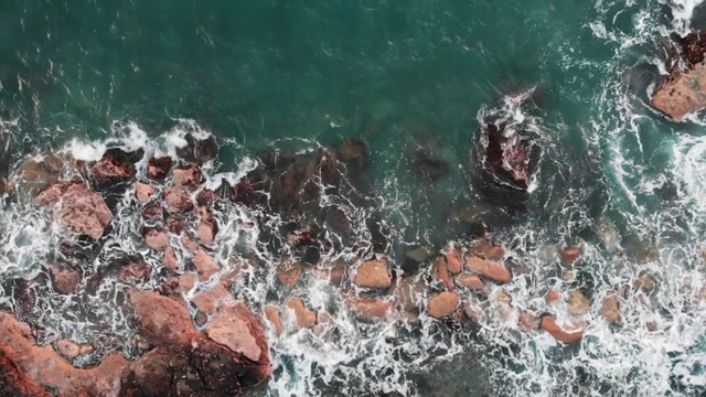 海浪撞击岩石和溅水的鸟瞰图。无人机的清澈的蓝色海水与白色泡沫视频素材