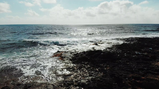 航拍海浪拍打着岩石海滩溅起的浪花。蓝天和地平线上的阳光路。在一个有风的日子大海。视频素材