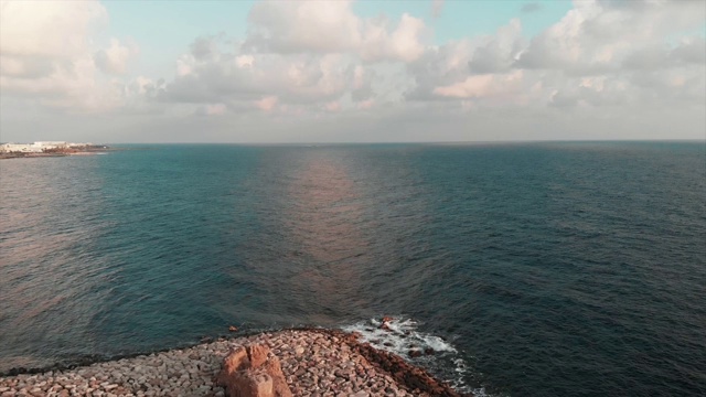 海面鸟瞰图与小波浪击中岩石海滩在阳光明媚的夏日与蓝天在地平线上视频素材