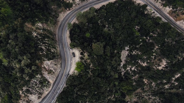 空中拍摄的森林在山区，蜿蜒的道路和黑色汽车(圣安妮塔峡谷，加利福尼亚，美国)视频素材