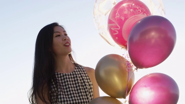 快乐的亚洲女孩圈与“生日快乐”气球从屋顶聚会日落，没有地平线。缓慢的运动。红色摄像机拍摄。视频素材