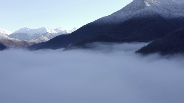 无人机飞过云雾之上的公路，到达覆盖着冬季森林和雪峰的高山。美丽的空中景观山峰和清澈的天空背景视频素材