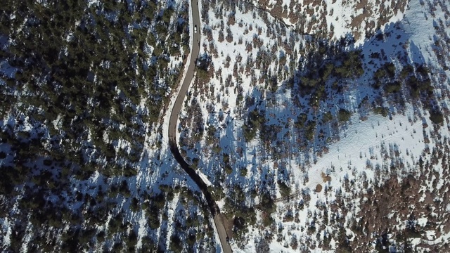 在恶劣天气下，俯视图无人机在弯曲的道路、风山和覆盖着积雪的森林上空飞行。视频素材