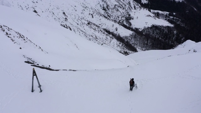 在冬季度假村的雪坡上，徒步者从空中无人机俯瞰山景。滑雪者在雪山旅游的寒假鸟瞰图。冬季登山和徒步旅行视频素材