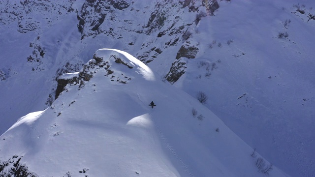 滑雪板与滑雪板行走在雪山山顶无人机的观点。滑雪板在雪峰上升起，骑在下坡上。冬天的山旅游。冬季极限运动视频素材