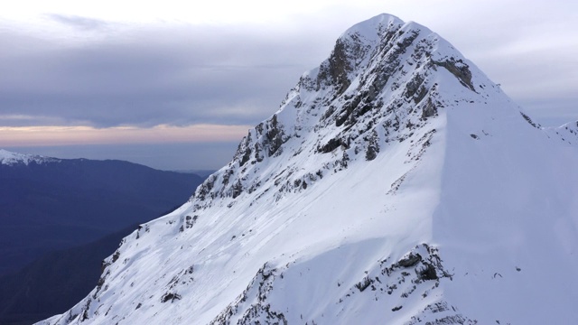 冬季的山峰和雪峰从上面的无人机飞行。空中景观雪山在冬季山谷。冬季景观山脉与雪峰在多云的天空视频素材