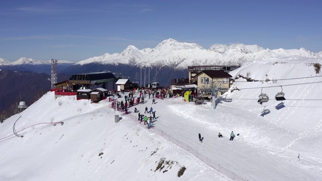 冬季度假村雪山鸟瞰图。男子在雪坡上用滑雪板滑雪。无人机拍摄雪山山顶上用于运输滑雪者和滑雪板的滑雪缆车站视频素材