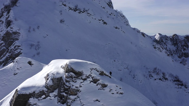 鸟瞰图滑雪板与雪山雪峰。无人机视图滑雪板攀登雪山山顶极限骑在斜坡上。冬天去雪山远足。冬季运动视频素材